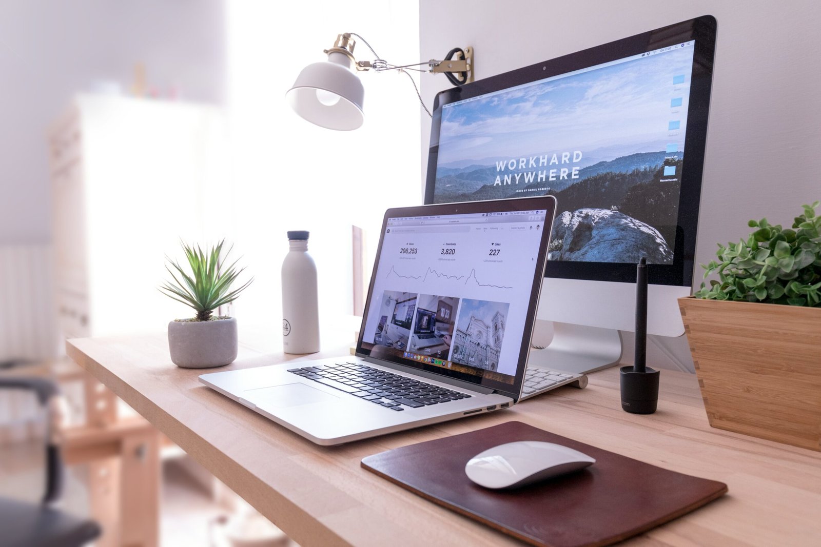 Home office setup with laptop, second screen showing a scenic landscape, and plants