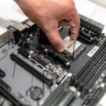 Hand installing or removing a CPU from a motherboard, showing the pins of the CPU.